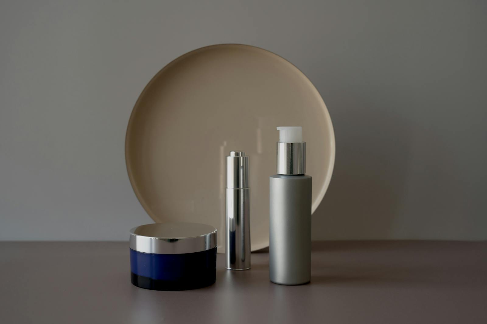 Trois soins cosmétiques (pot de crème, sérum et flacon) posés sur un fond neutre et épuré, illustration d'un guide pour lire la formule d'un cosmétique au CBD et bien le choisir.