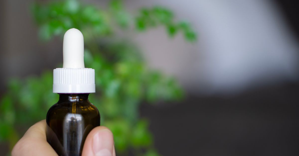 Flacon compte-gouttes d'huile de CBD tenu à la main devant une plante verte, illustrant les cannabinoïdes naturels CBD, CBG et CBN