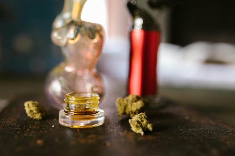 Bocal en verre contenant un concentré de cannabis (résine) entouré de bourgeons séchés sur une table — illustration du comparatif fleurs CBD vs résines CBD